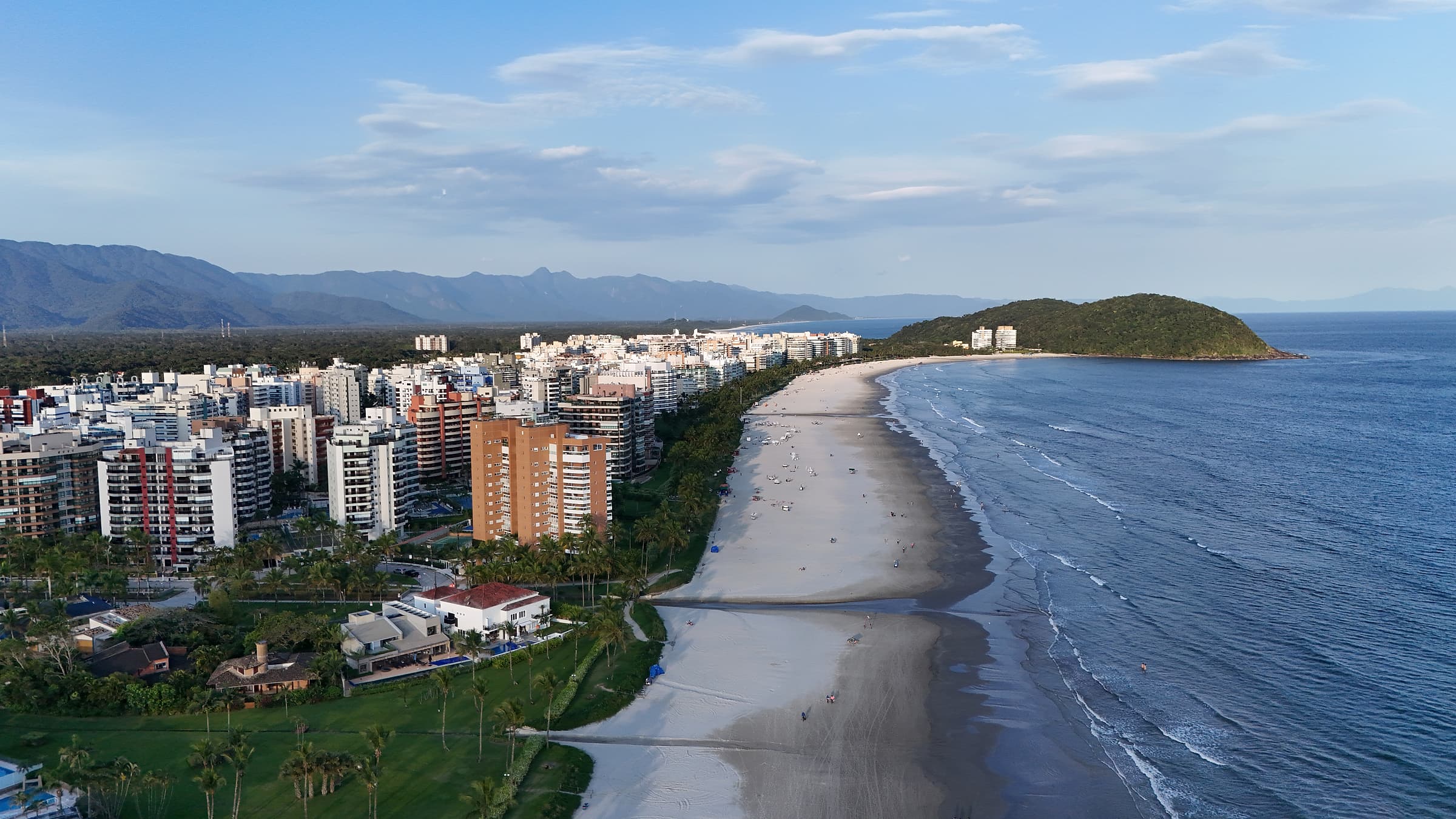 Vista aérea da Riviera de São Lourenço no fim de tarde: a orla, os prédios, a Serra do Mar e o morro ao fundo